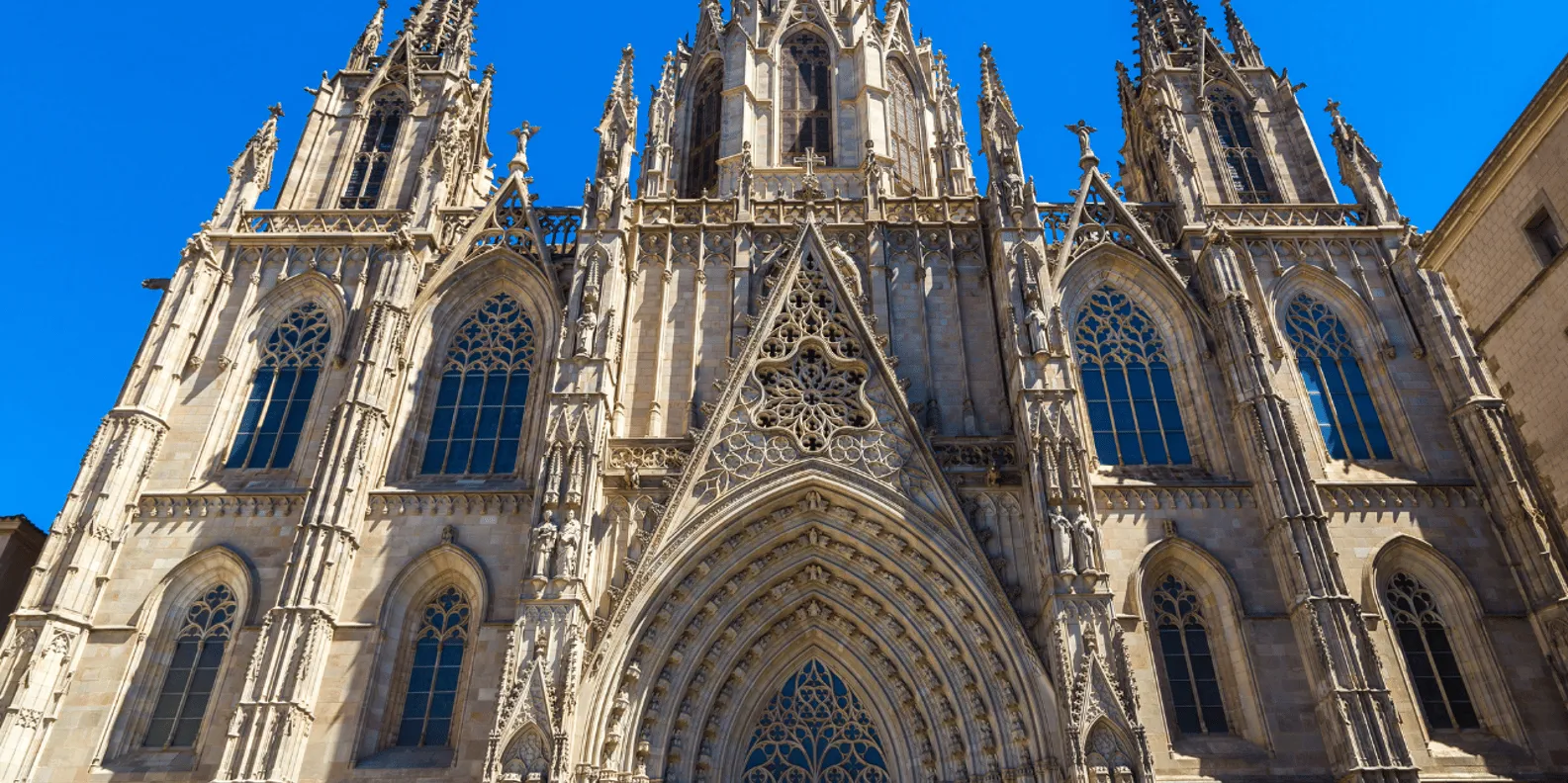 The ornate neo-Gothic facade and pointed towers of Barcelona Cathedral against a clear blue sky