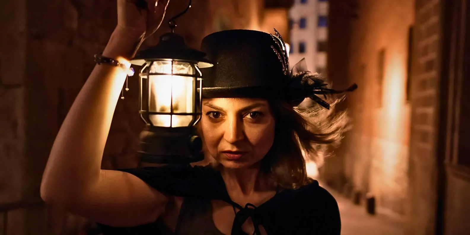 A costumed guide holding a glowing lantern on an evening ghost tour in a dark Gothic Quarter alley in Barcelona