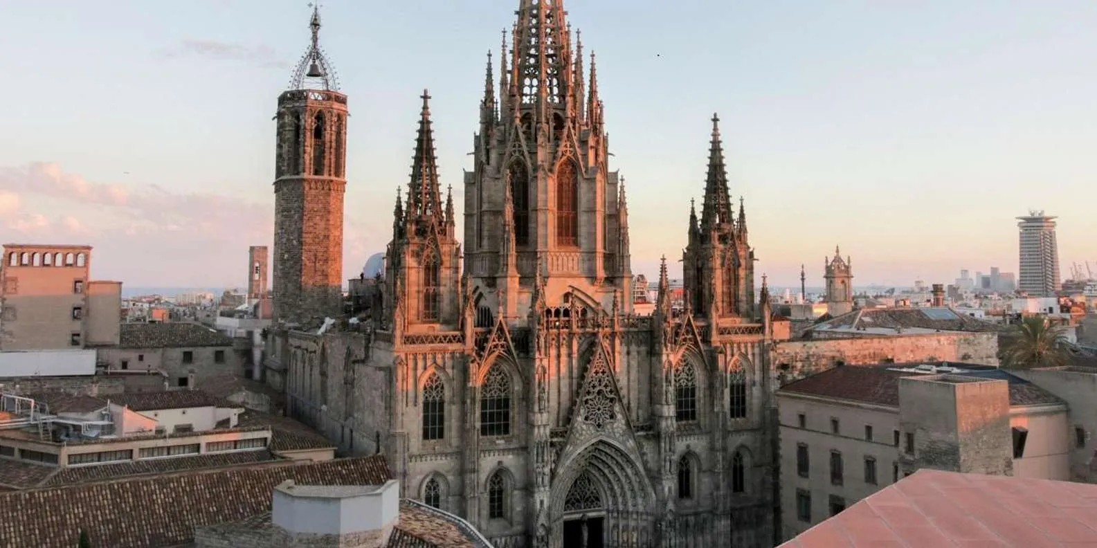 Barcelona Cathedral (La Seu) and the Gothic Quarter rooftops glowing at golden hour, with the Mediterranean in the distance